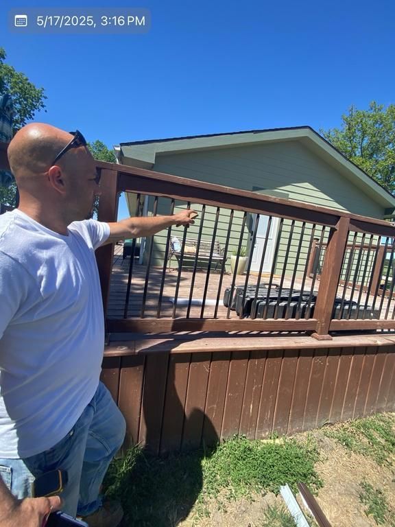 A man is pointing at a wooden railing in front of a house.