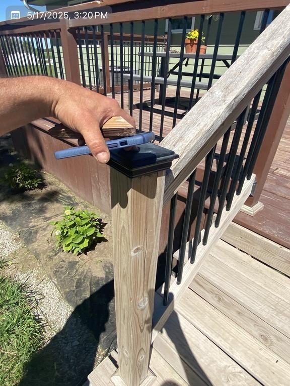 A person is holding a brush on a wooden railing on a deck.