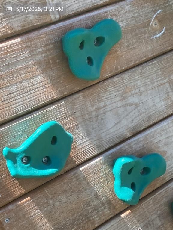 Three green climbing holds are sitting on a wooden surface
