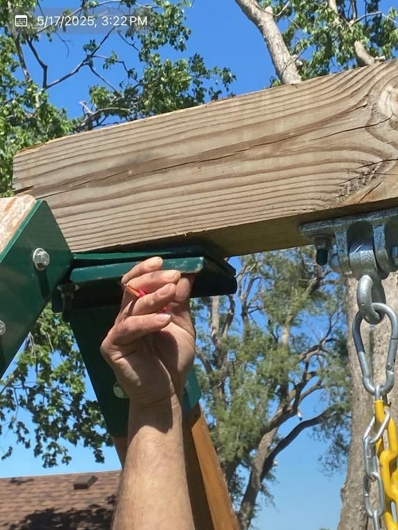 A person 's hand is reaching up to a wooden beam with trees in the background