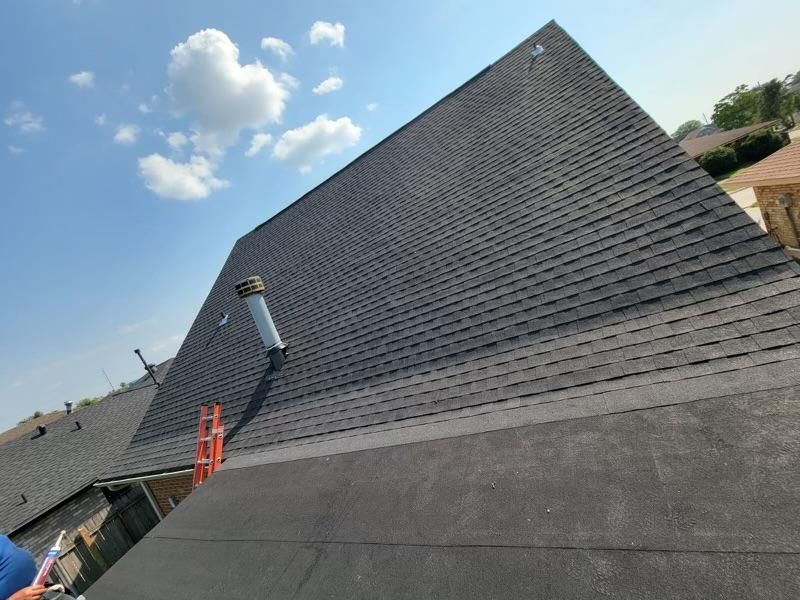A man is standing on the roof of a house with a ladder.
