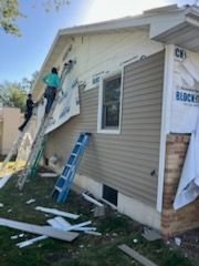 A man is standing on a ladder on the side of a house.