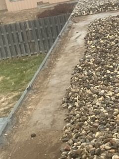 A pile of rocks on the side of a road next to a wooden fence.