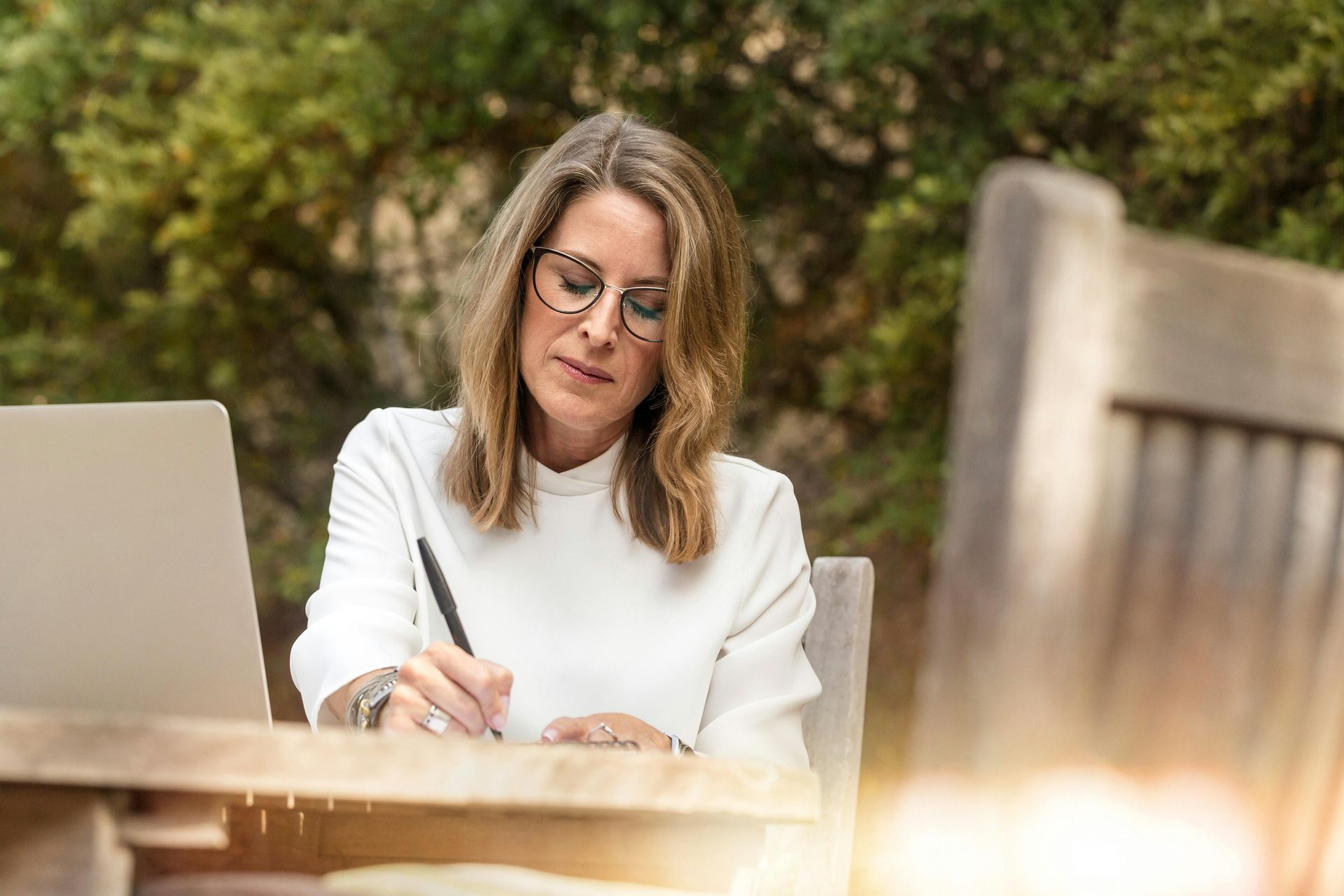 A woman is sitting at a table with a laptop and writing on a piece of paper.