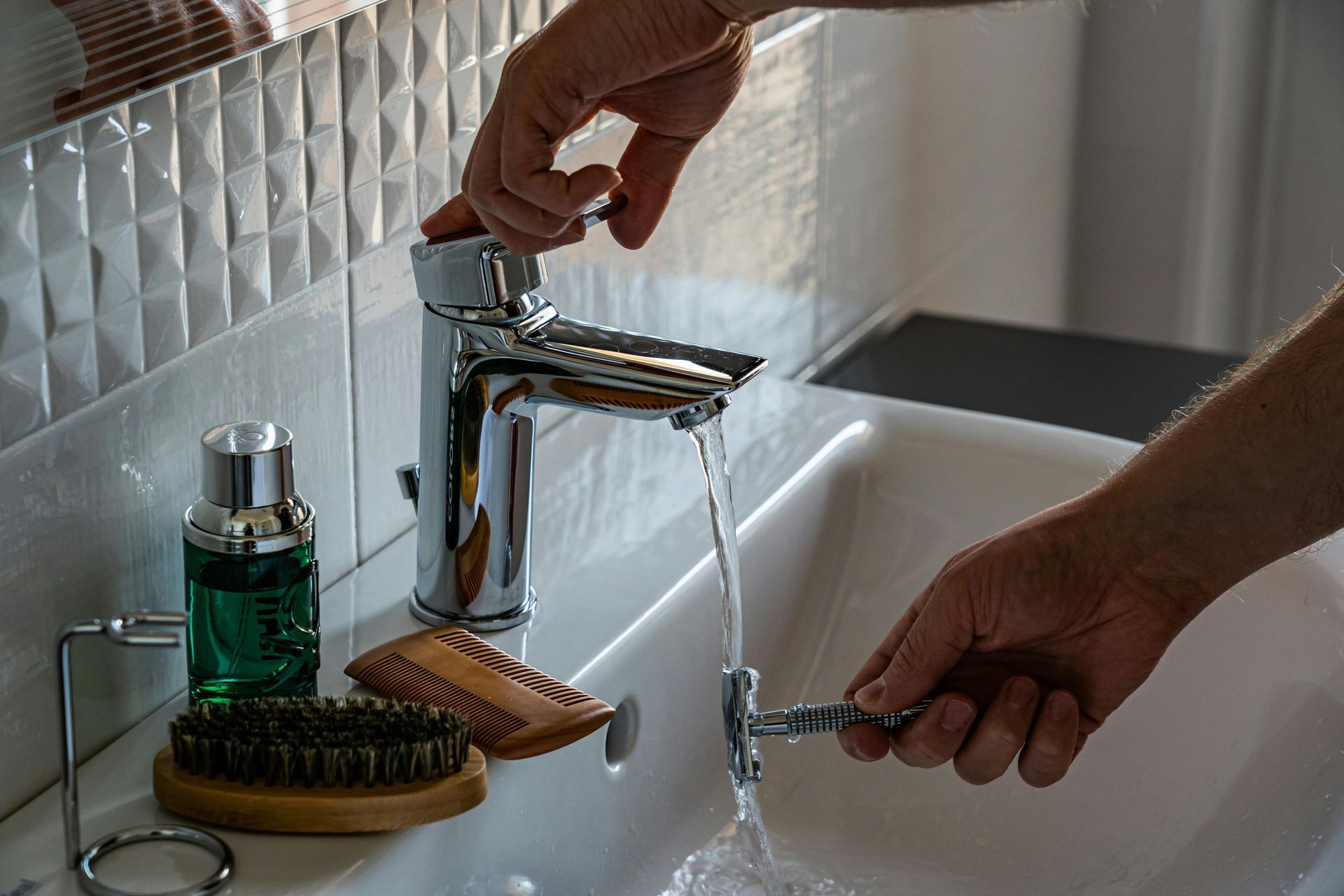 A person is washing a razor in a bathroom sink.