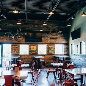 Restaurant interior with wooden walls, red chairs, and metal tables. Two bikes hang on the wall.