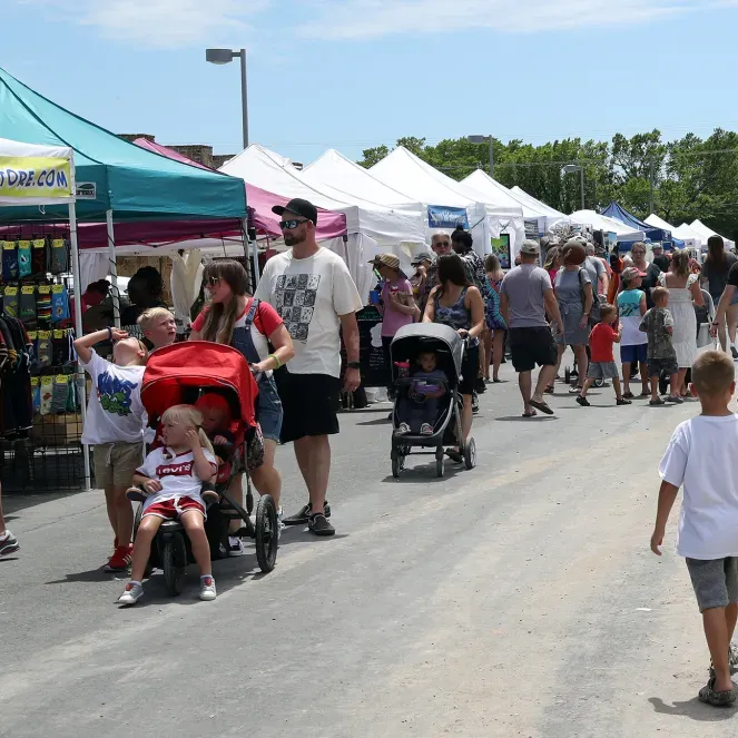 Outdoor market crowd with white tents and strollers along a sunny street