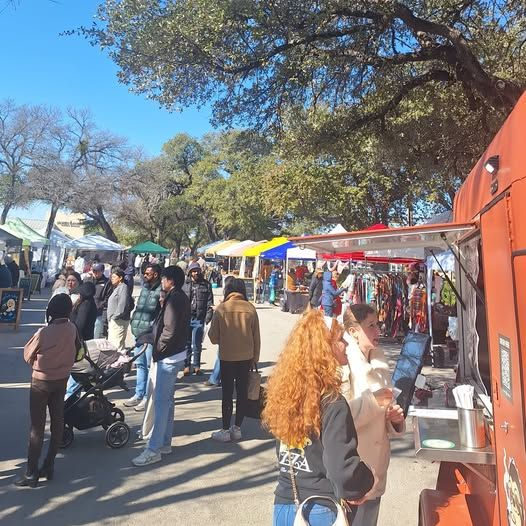 Outdoor market with food truck, vendors, and crowd under sunny, blue sky.