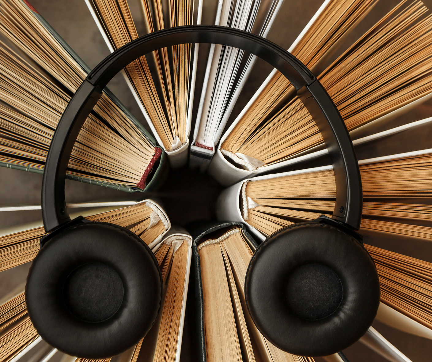 Black headphones resting on a fan of open books, top view.