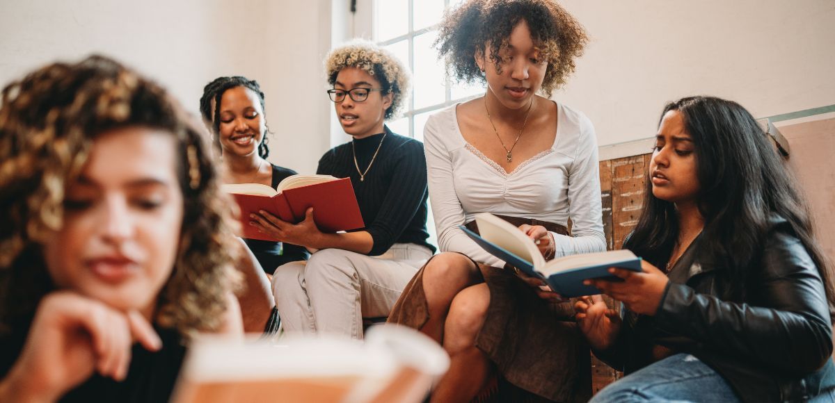 Five friends sitting together, reading and discussing books in a cozy living room.