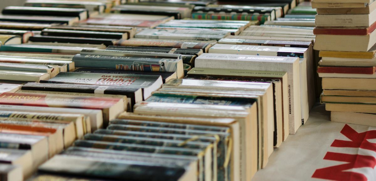 Rows of used books stacked on tables at an outdoor market, with a red star design on the ground