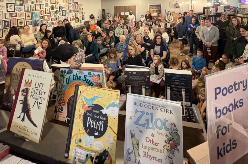 Crowded bookstore event with people posing behind colorful poetry books and signs.