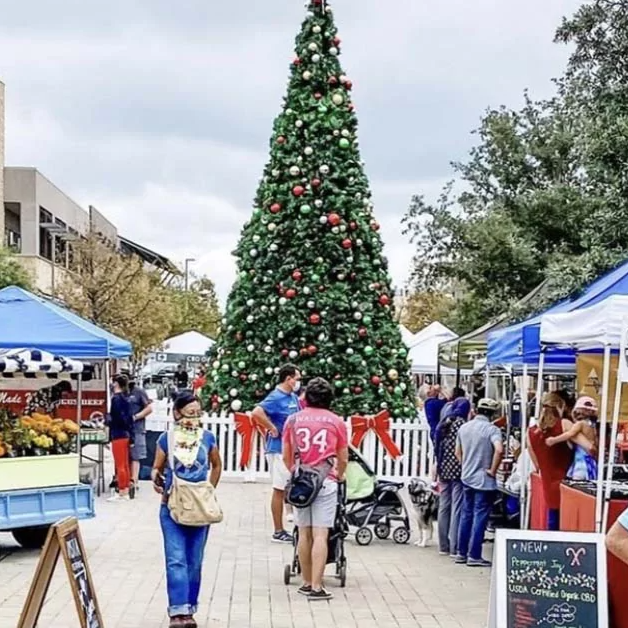 Outdoor Christmas market with large tree, vendors, shoppers, and a stroller.