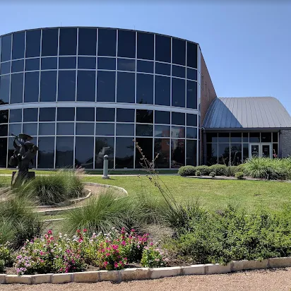 Modern building with curved glass facade, green lawn, and landscaping under a blue sky.