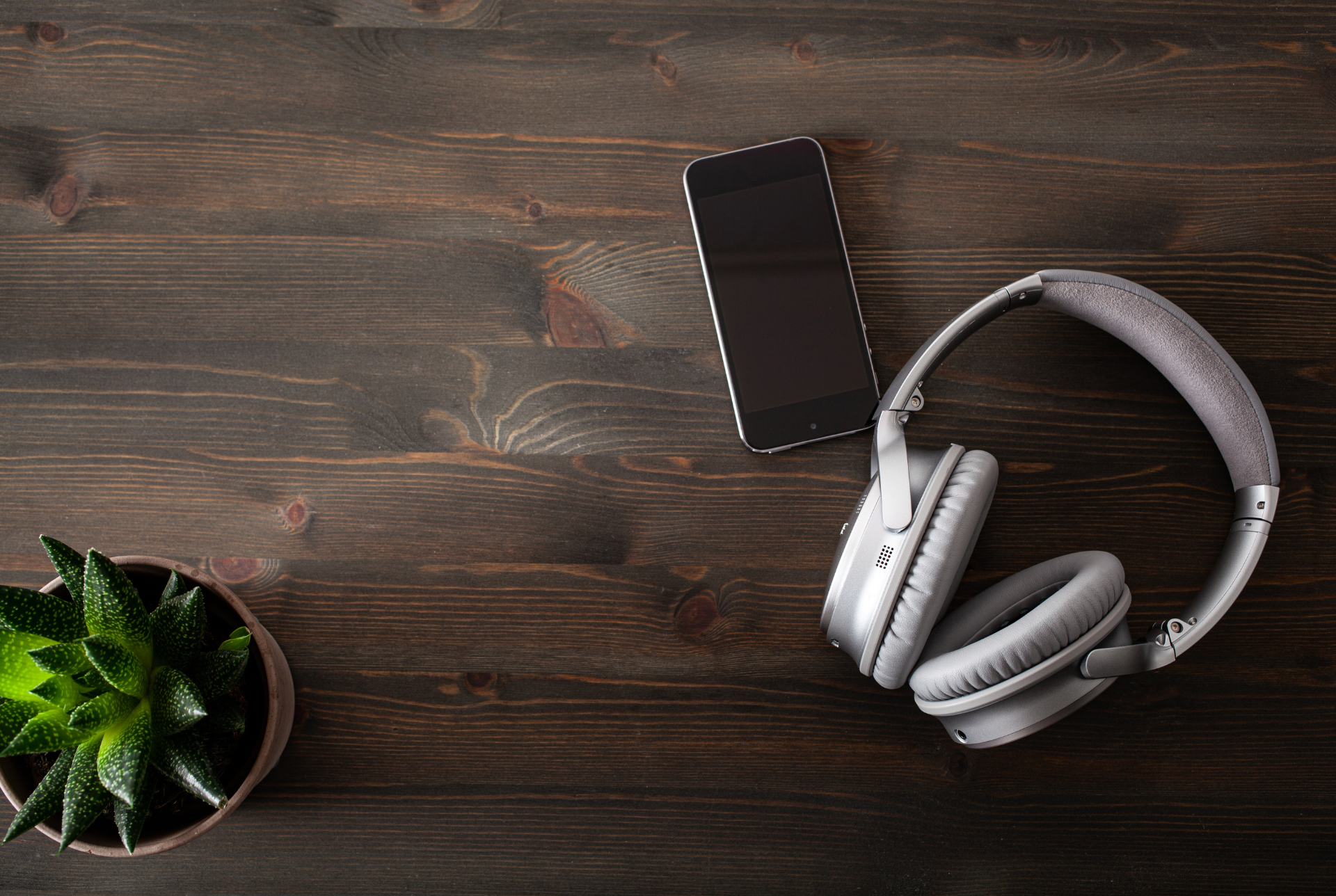 A pair of headphones and a cell phone on a wooden table.
