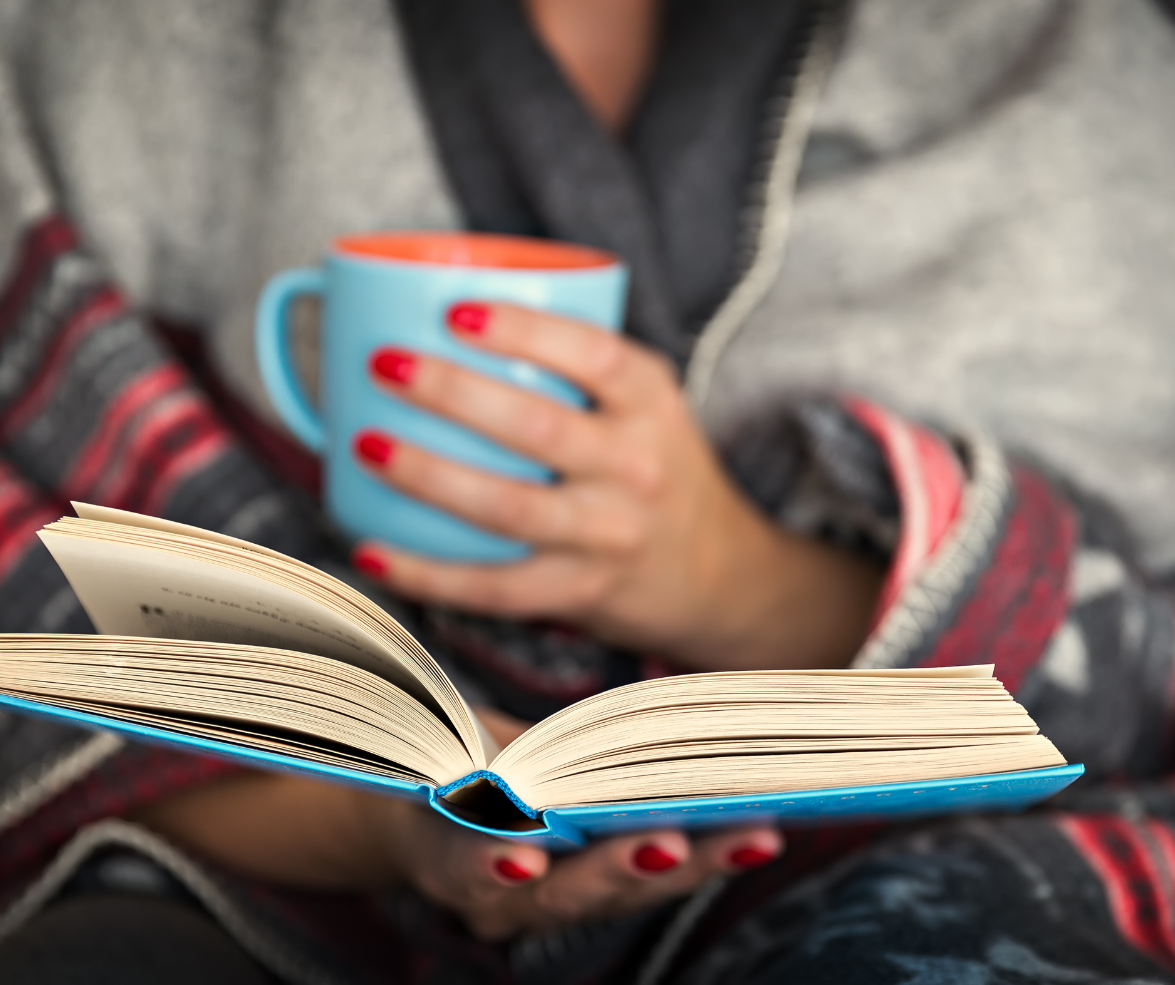 A woman is reading a book while holding a cup of coffee