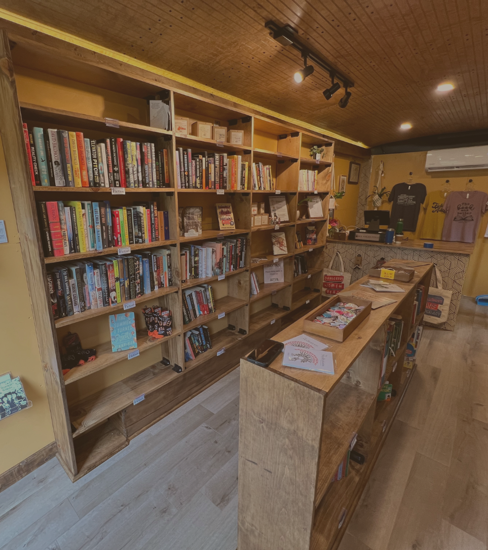 A warm-toned bookstore interior featuring wooden shelves filled with books and a service counter in the background.