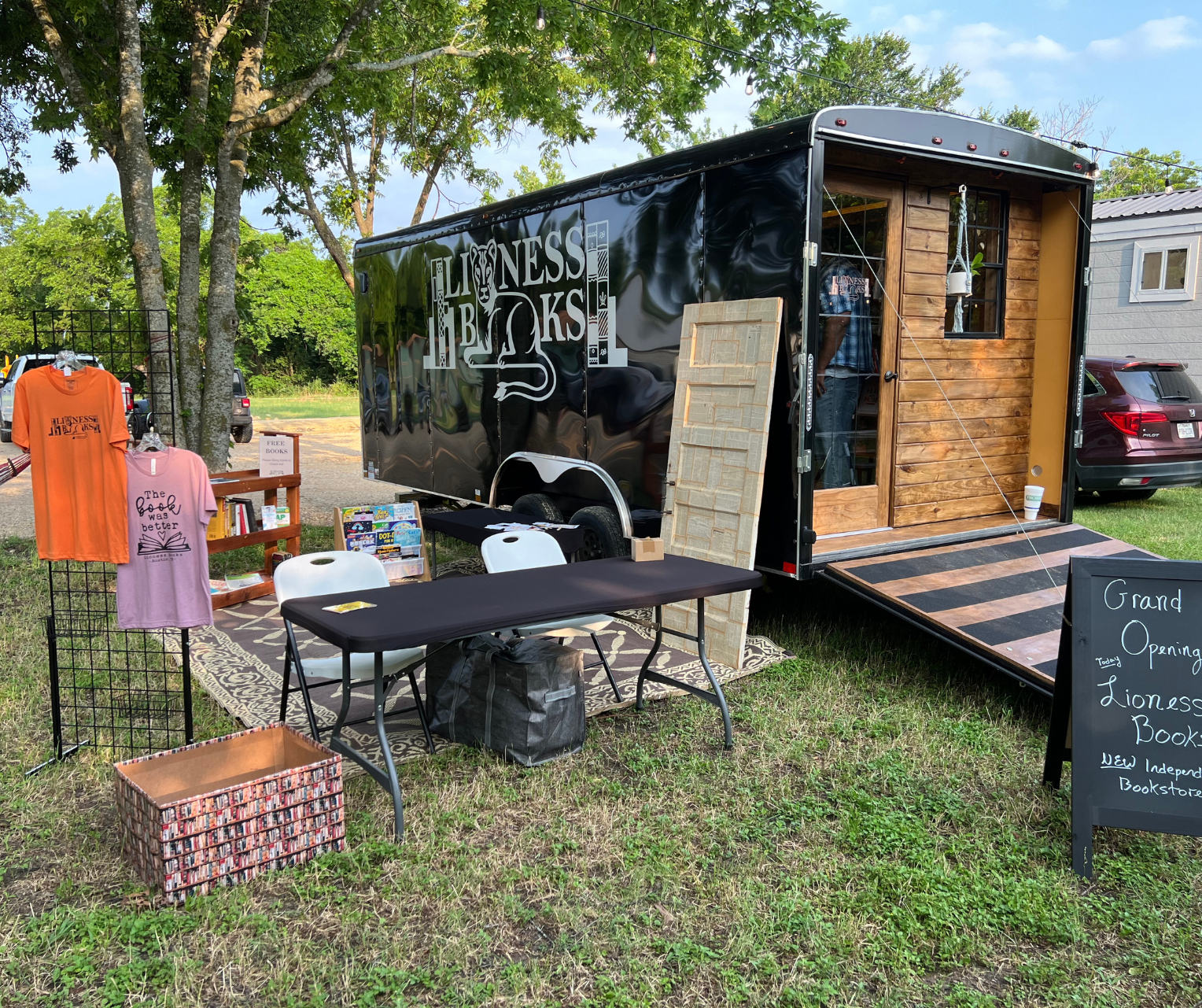 A black trailer is parked in the grass next to a table and chairs.