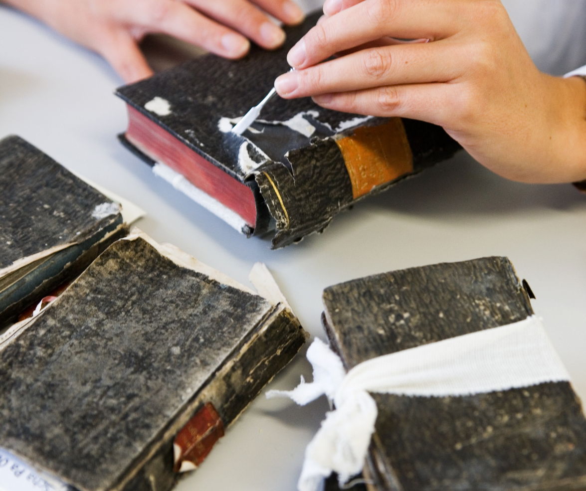 Hands working on a damaged book, applying glue. Other damaged books are on the table.