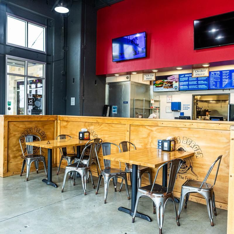 Modern café seating with metal tables and chairs beneath red walls and TVs