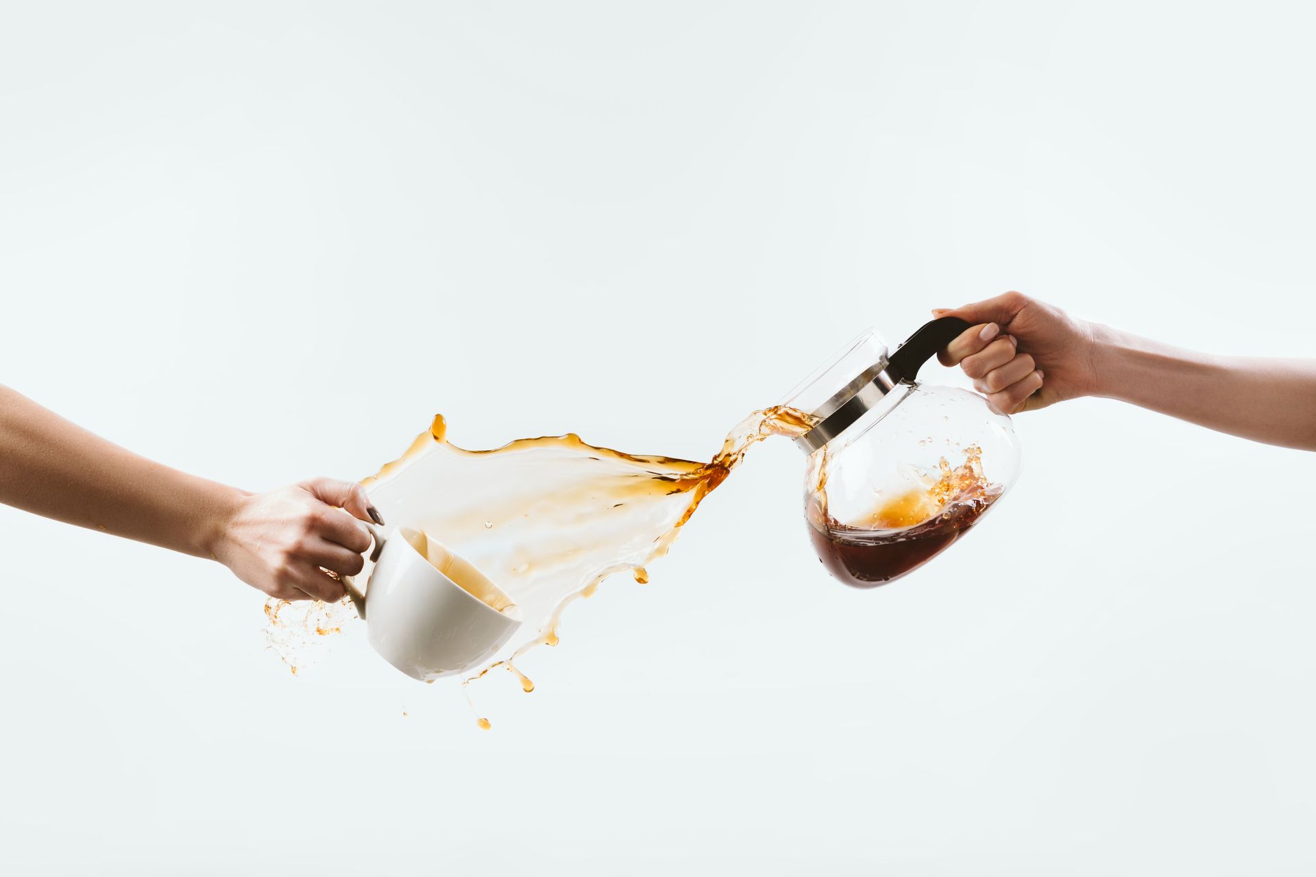 Hands pouring coffee from a carafe into a mug, coffee splashing.