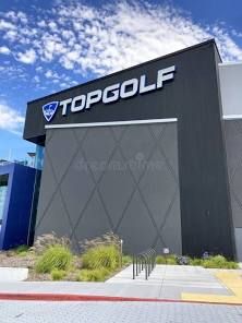 Topgolf building exterior with a gray facade, white sign, blue sky, and landscaping.