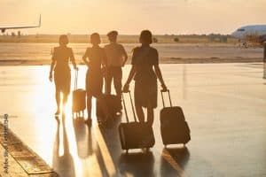 Four airline workers with luggage walking across an airport tarmac toward a setting sun.