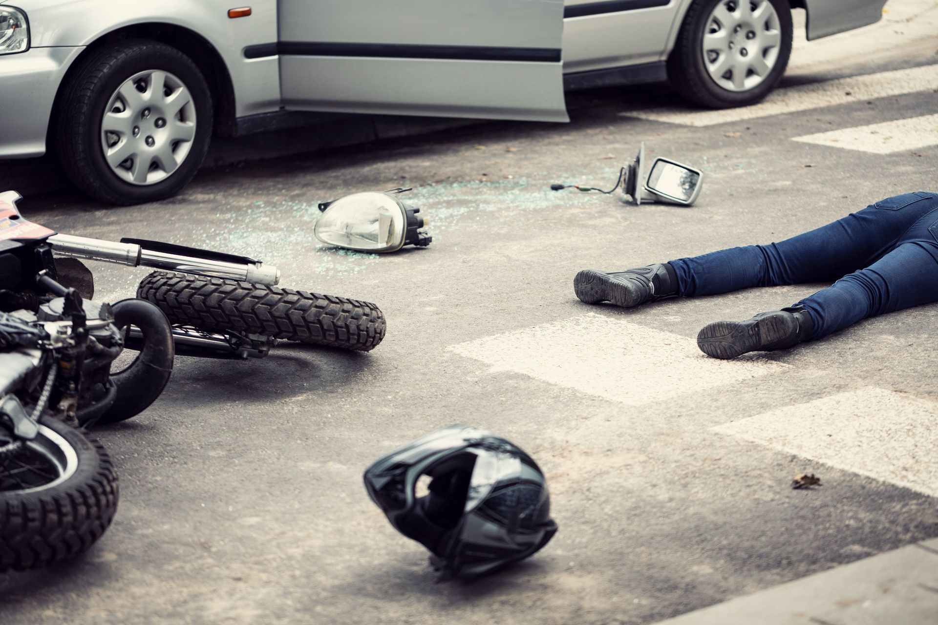 Car accident: a car and motorcycle on a street; person lying on the ground, helmet nearby.