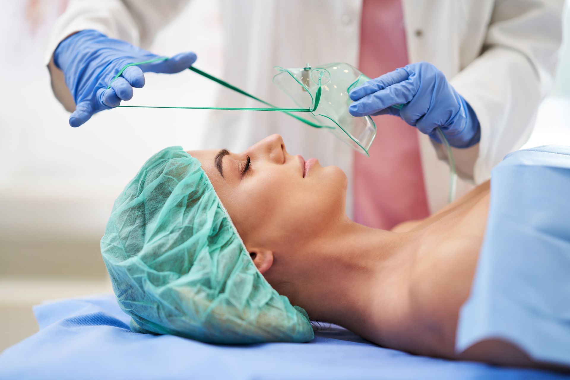 Woman receiving anesthesia in a medical setting; nurse adjusts oxygen mask.