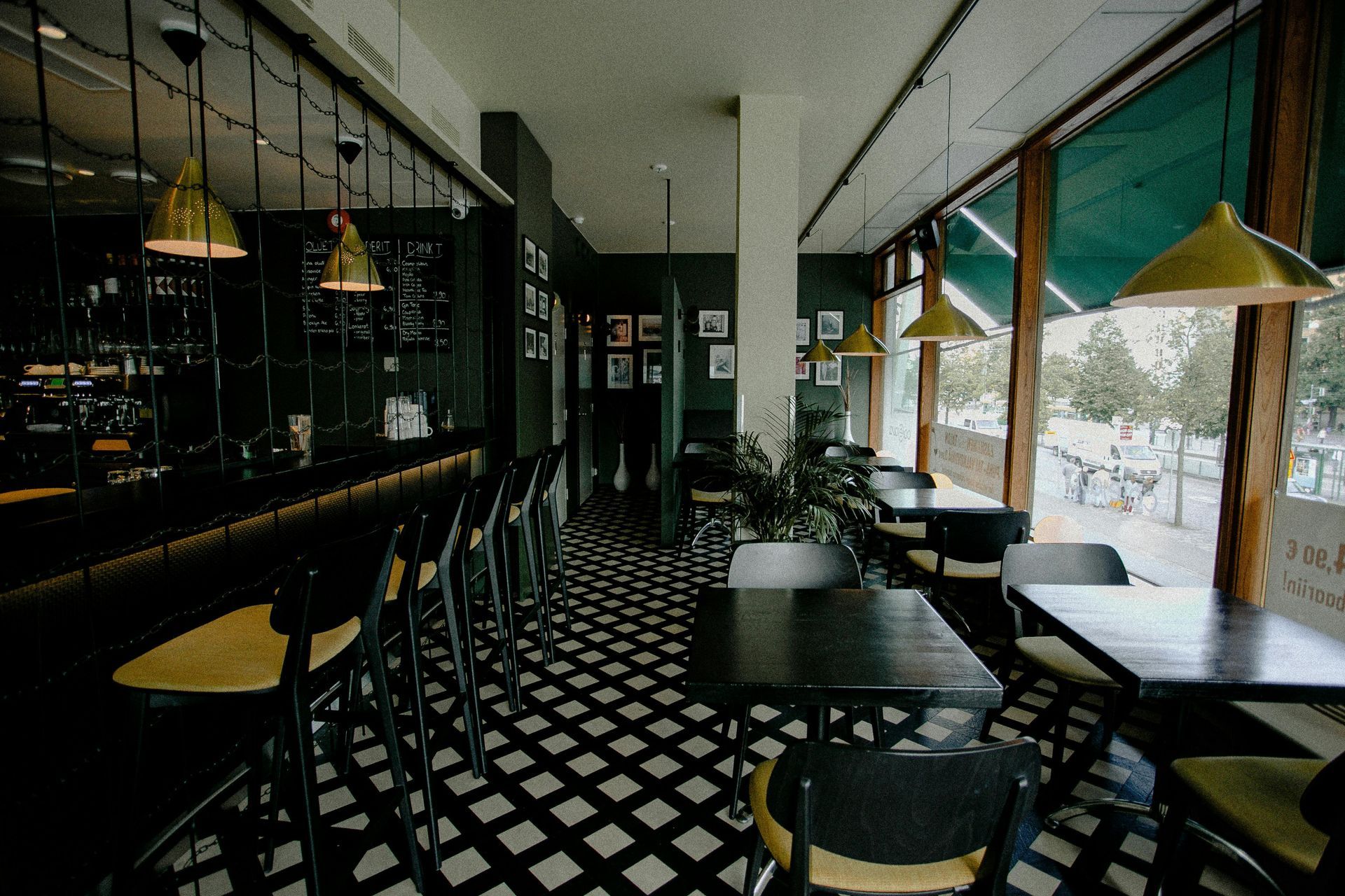 Interior view of a cafe with black and white tiled floor, dark green walls, and large windows.