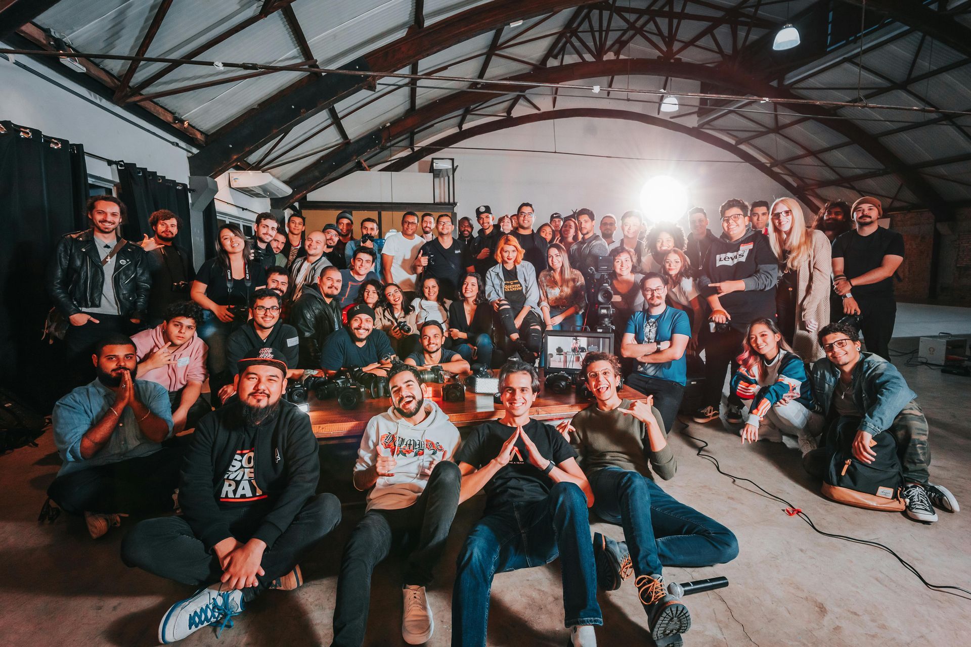 Large group of people smiling in an industrial space with exposed beams; some are seated.