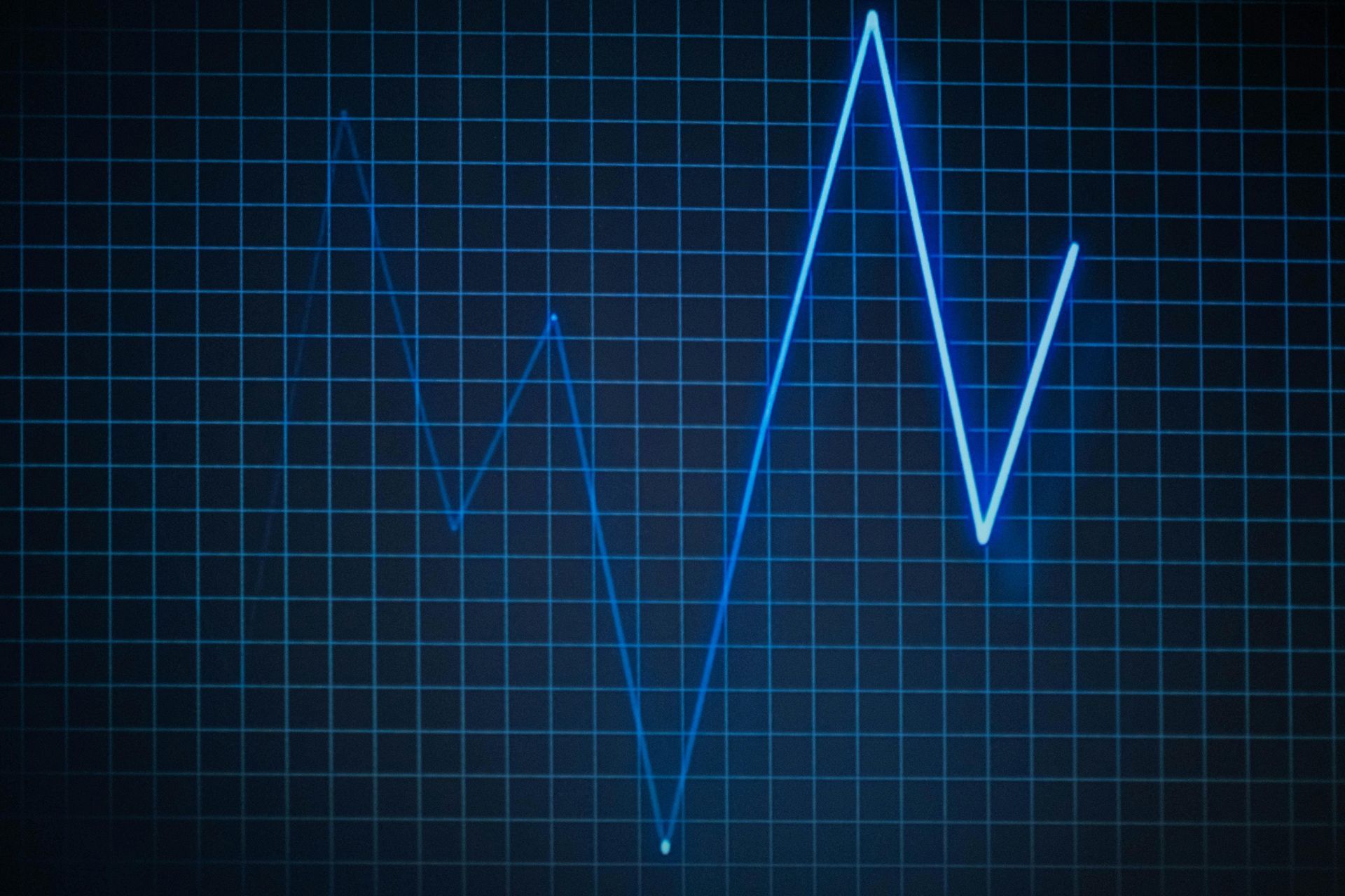 Blue, jagged line chart on a dark blue grid, suggesting fluctuating data.