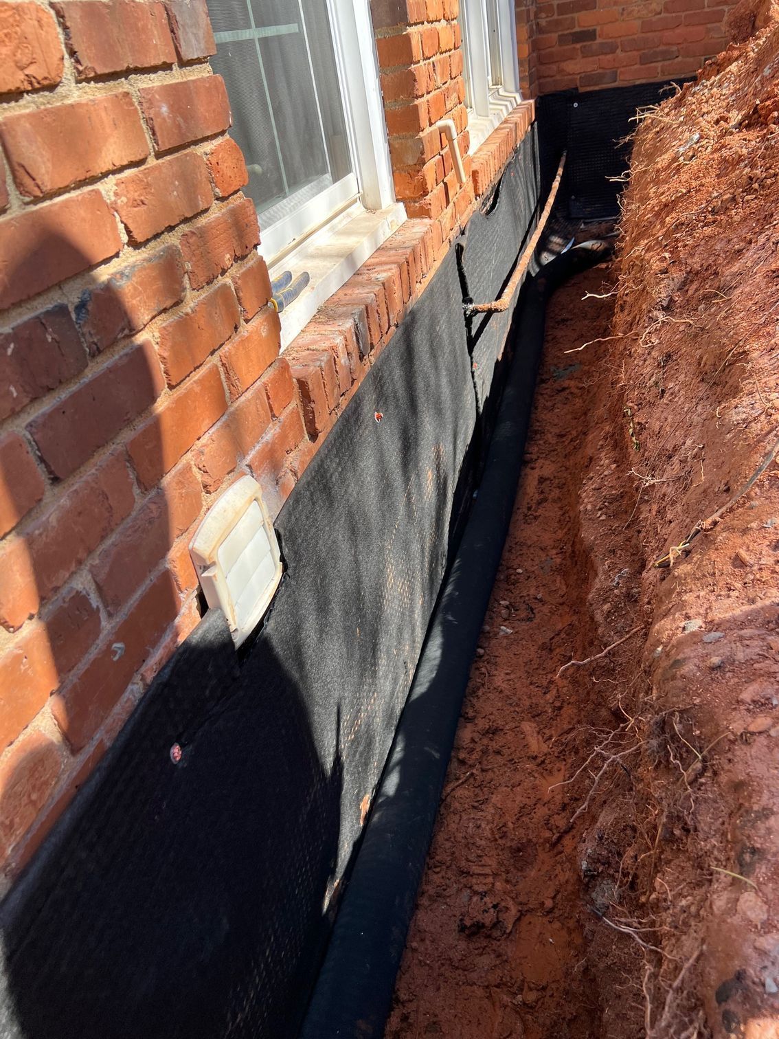 A drainage system is being installed on the side of a brick building.