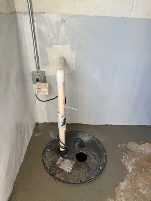 A sump pump is sitting in a basement next to a wall.