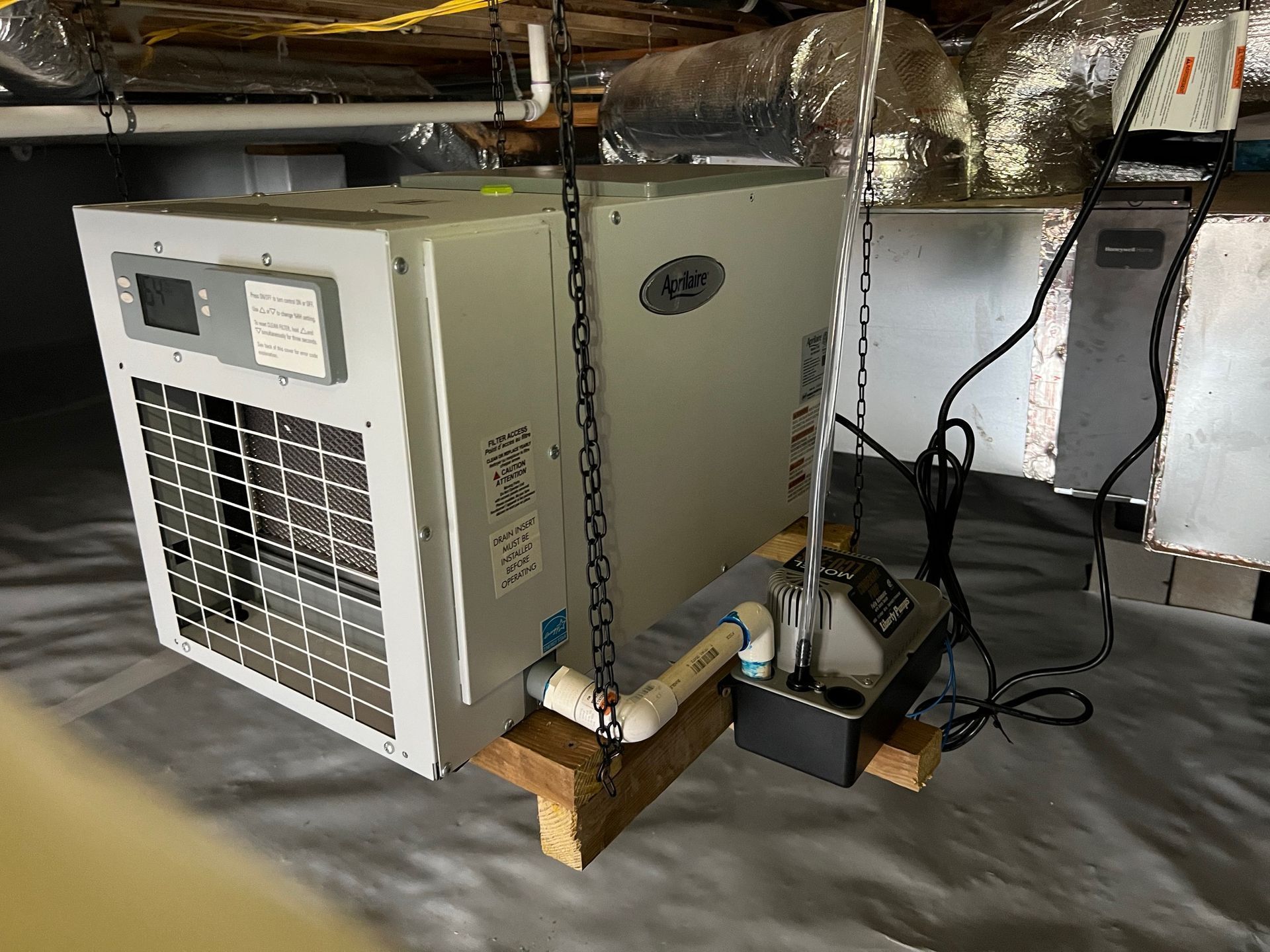 A white air conditioner is sitting on a wooden platform in a basement.