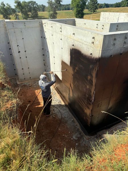 A man is spraying black paint on a concrete wall