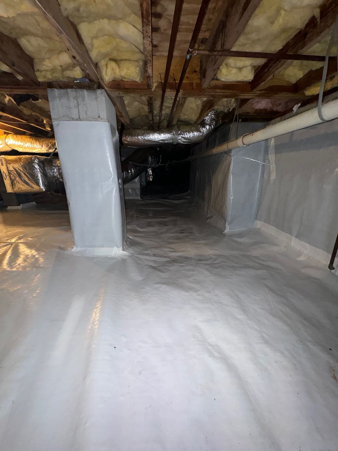 A basement with a lot of insulation and plastic covering the floor.