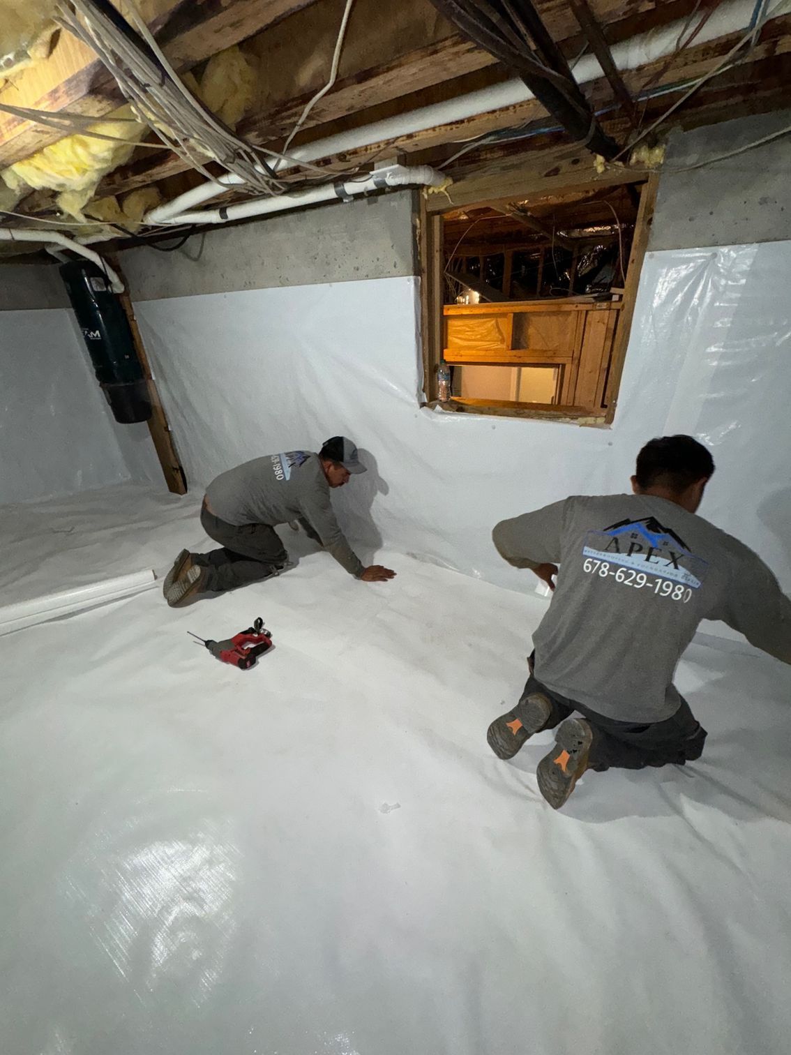 Two men are kneeling on the floor of a basement.