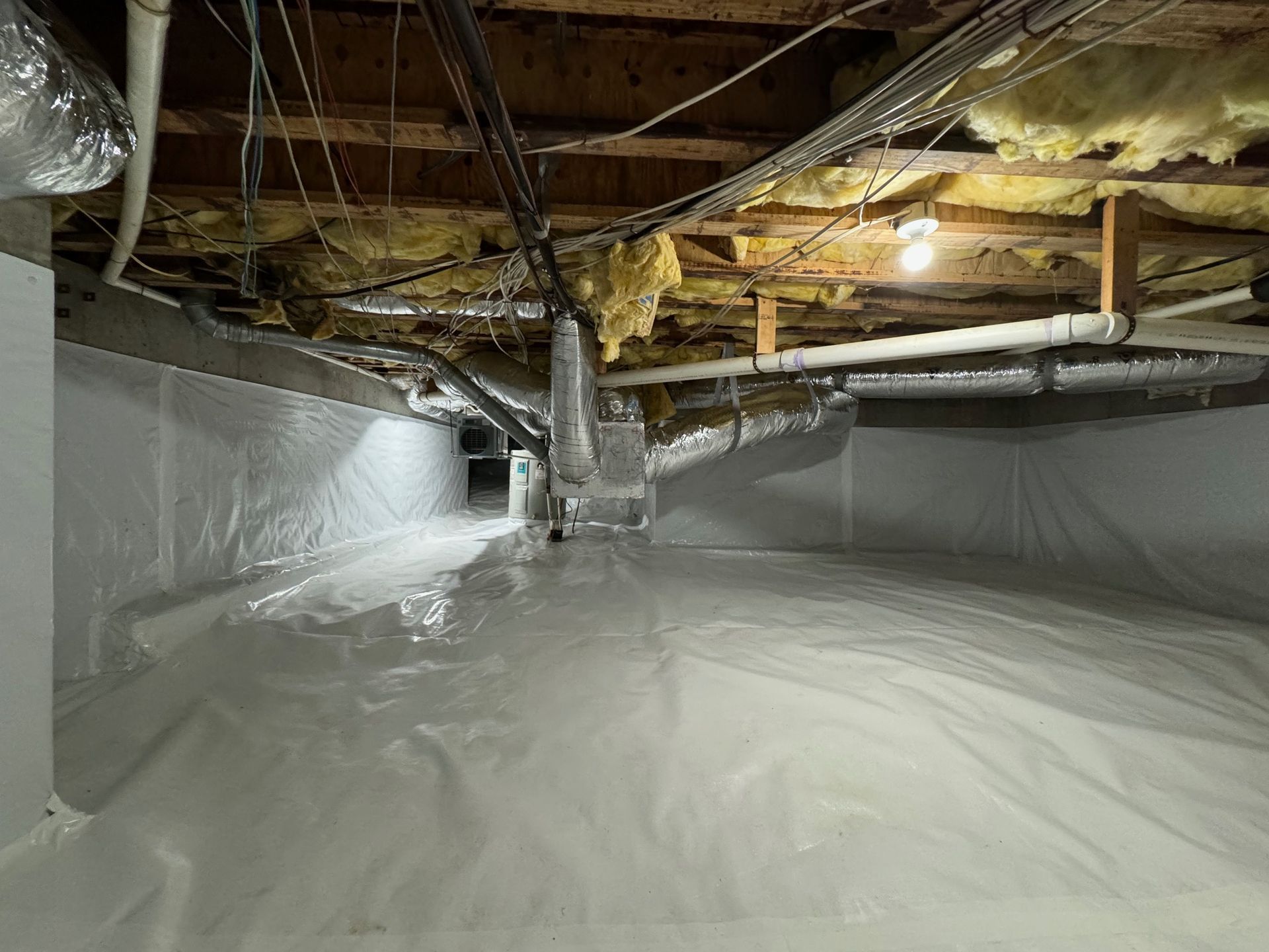 The ceiling of a basement with a lot of pipes and insulation.
