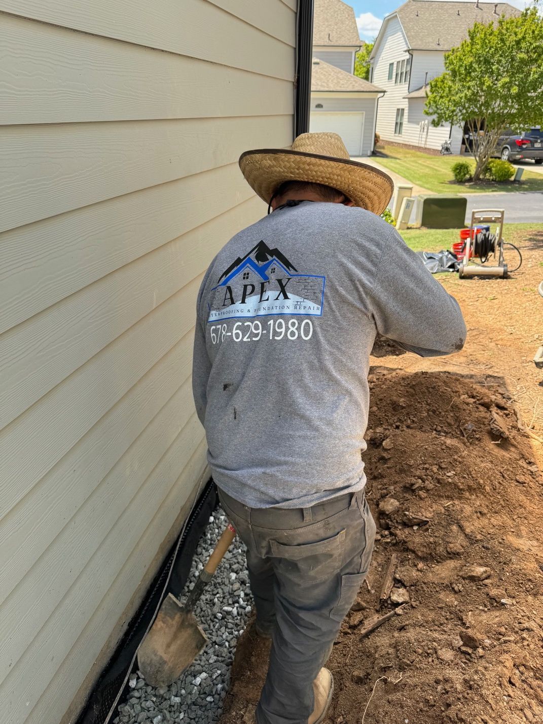 A man wearing a straw hat and a grey shirt is digging in the dirt.