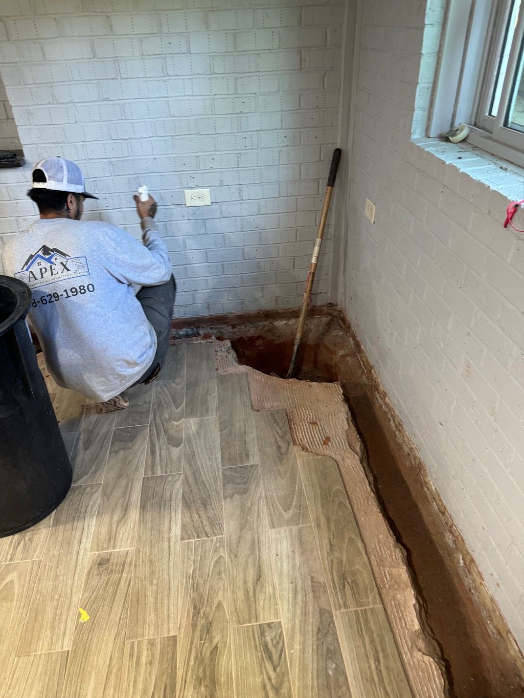 A man is kneeling down in a room next to a hole in the floor.