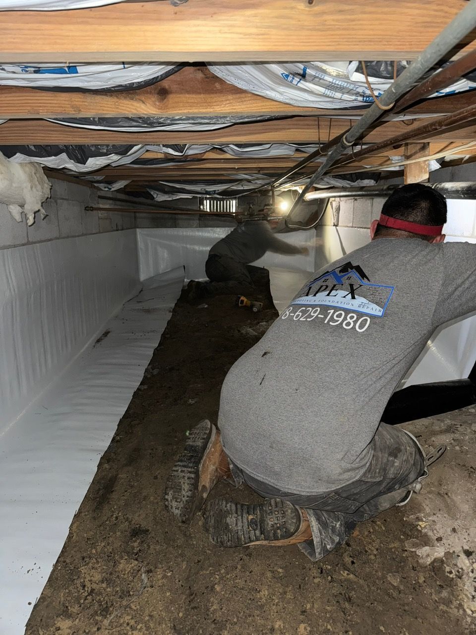 A man in a gray shirt is kneeling down in a basement.