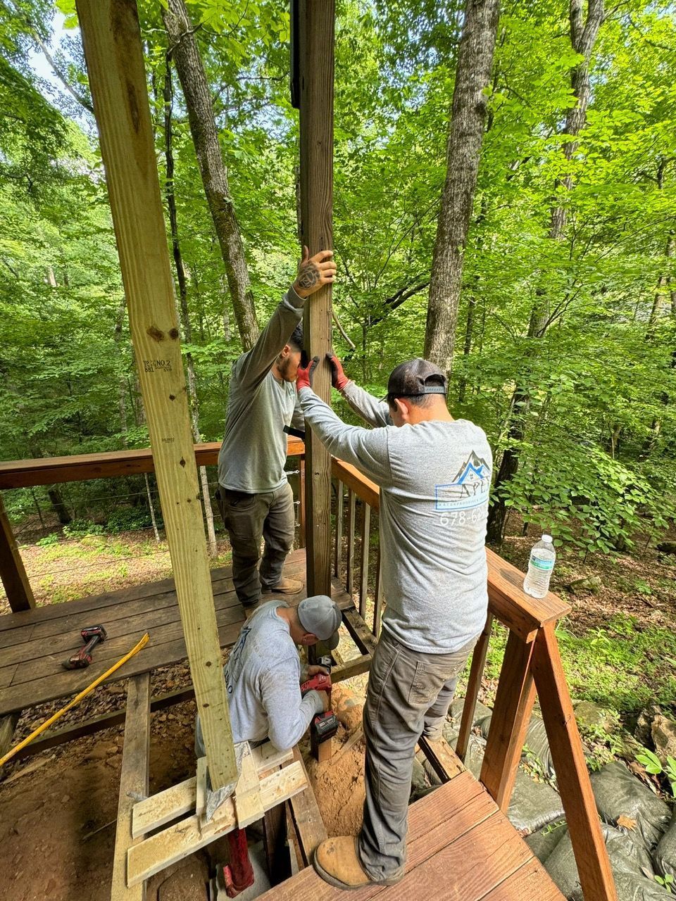 Two men are working on a wooden deck in the woods.