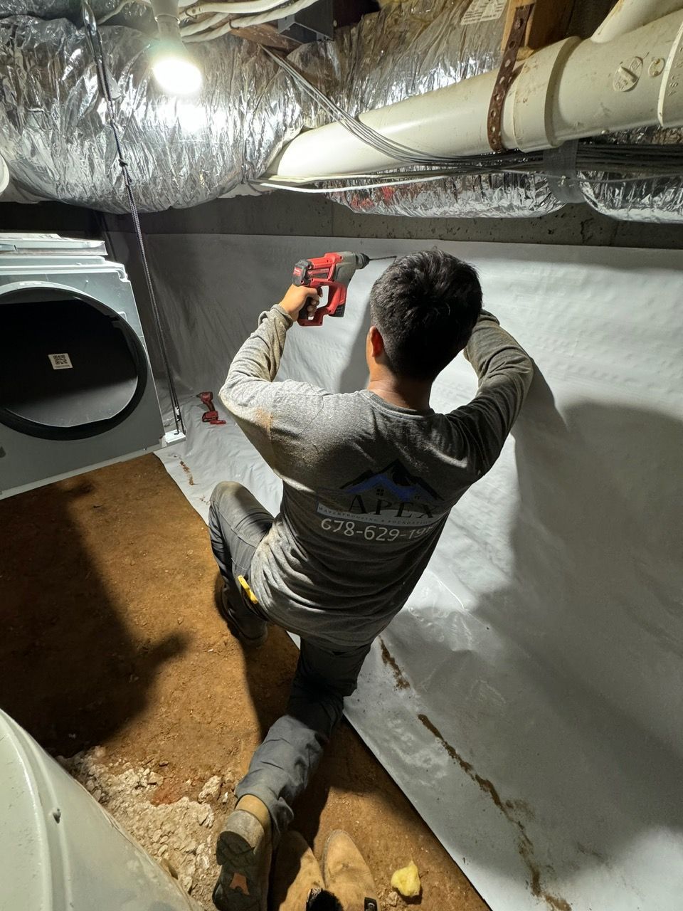 A man is kneeling down in a basement using a drill.