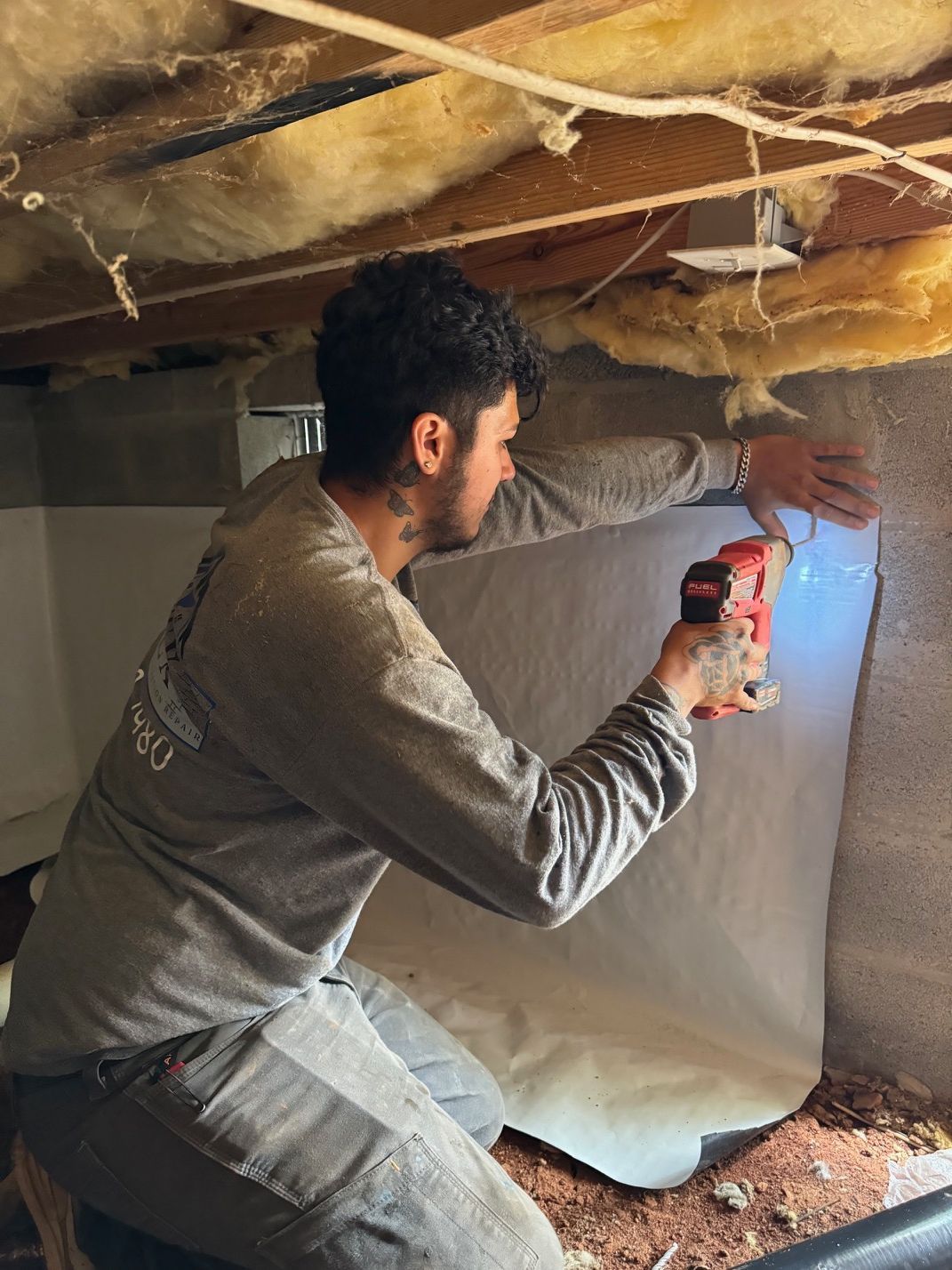 A man is kneeling down in a basement holding a drill.