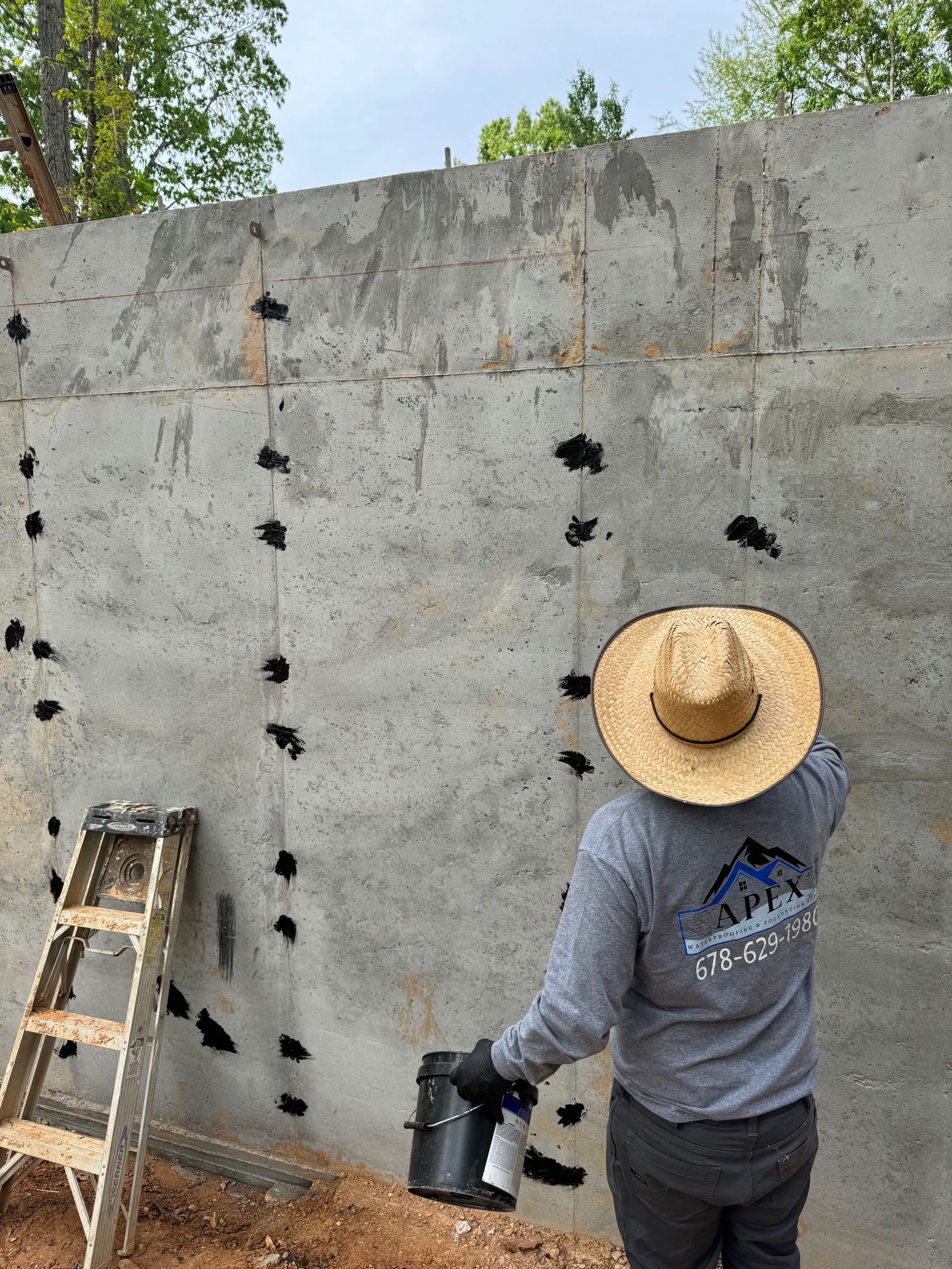A woman in a hat is spraying paint on a concrete wall.