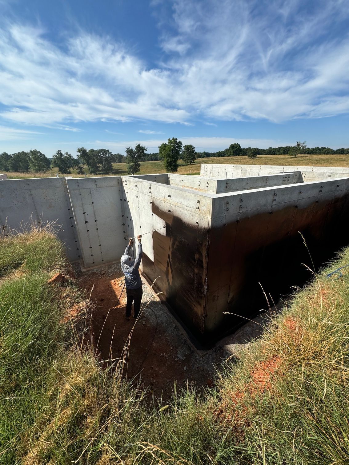 A man is digging a hole in the ground next to a concrete wall.