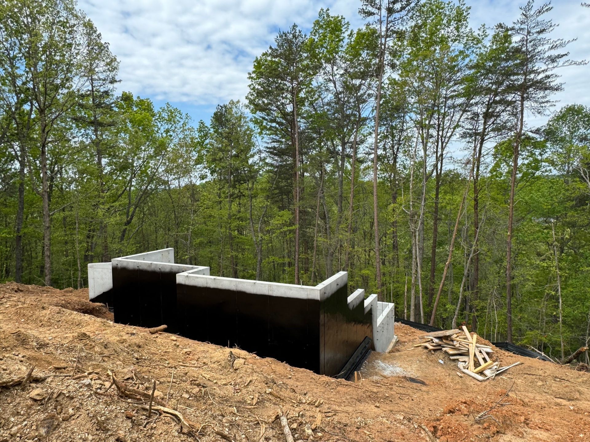 A building is being built on top of a dirt hill in the middle of a forest.