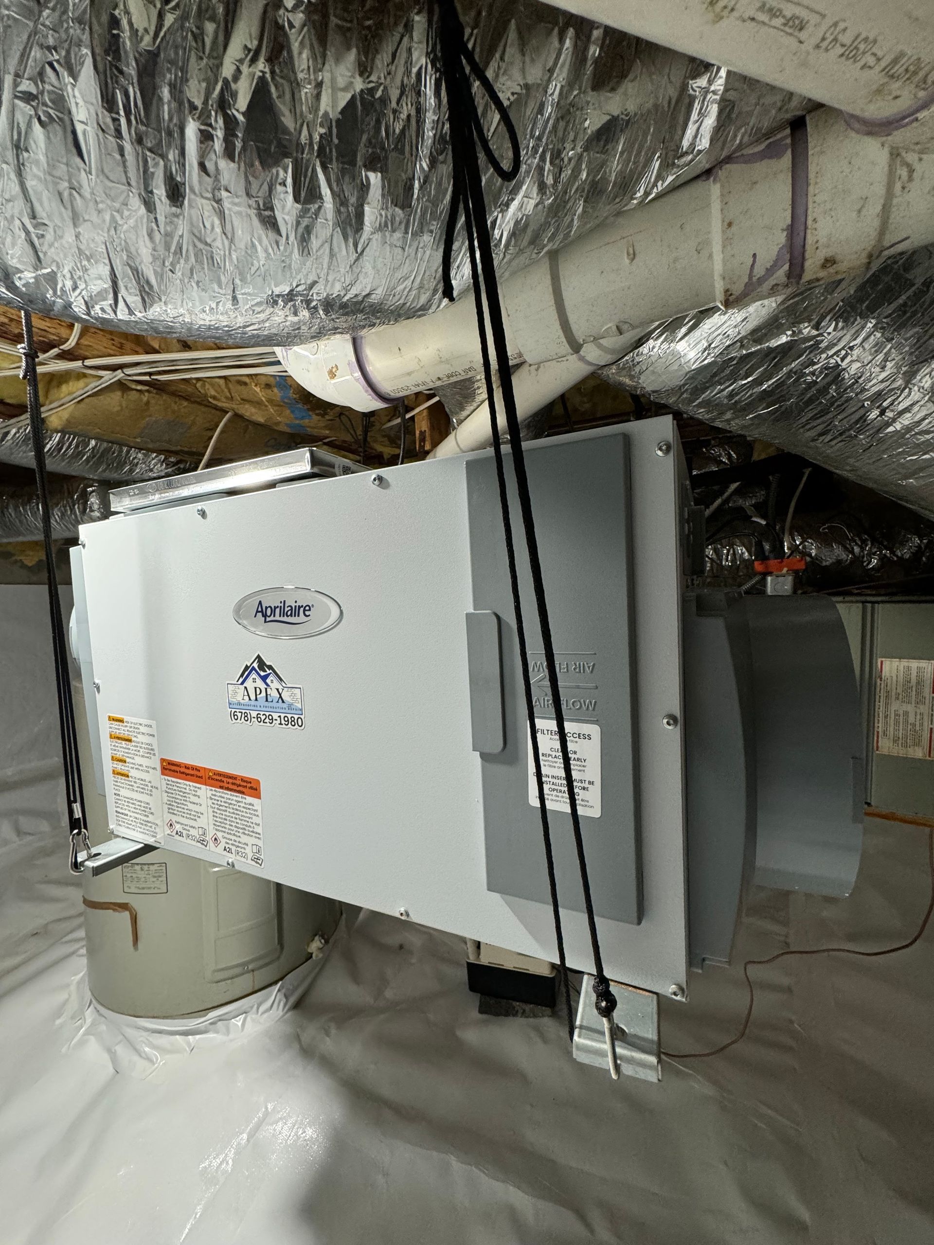 White humidifier unit in a crawlspace, hanging from ceiling.