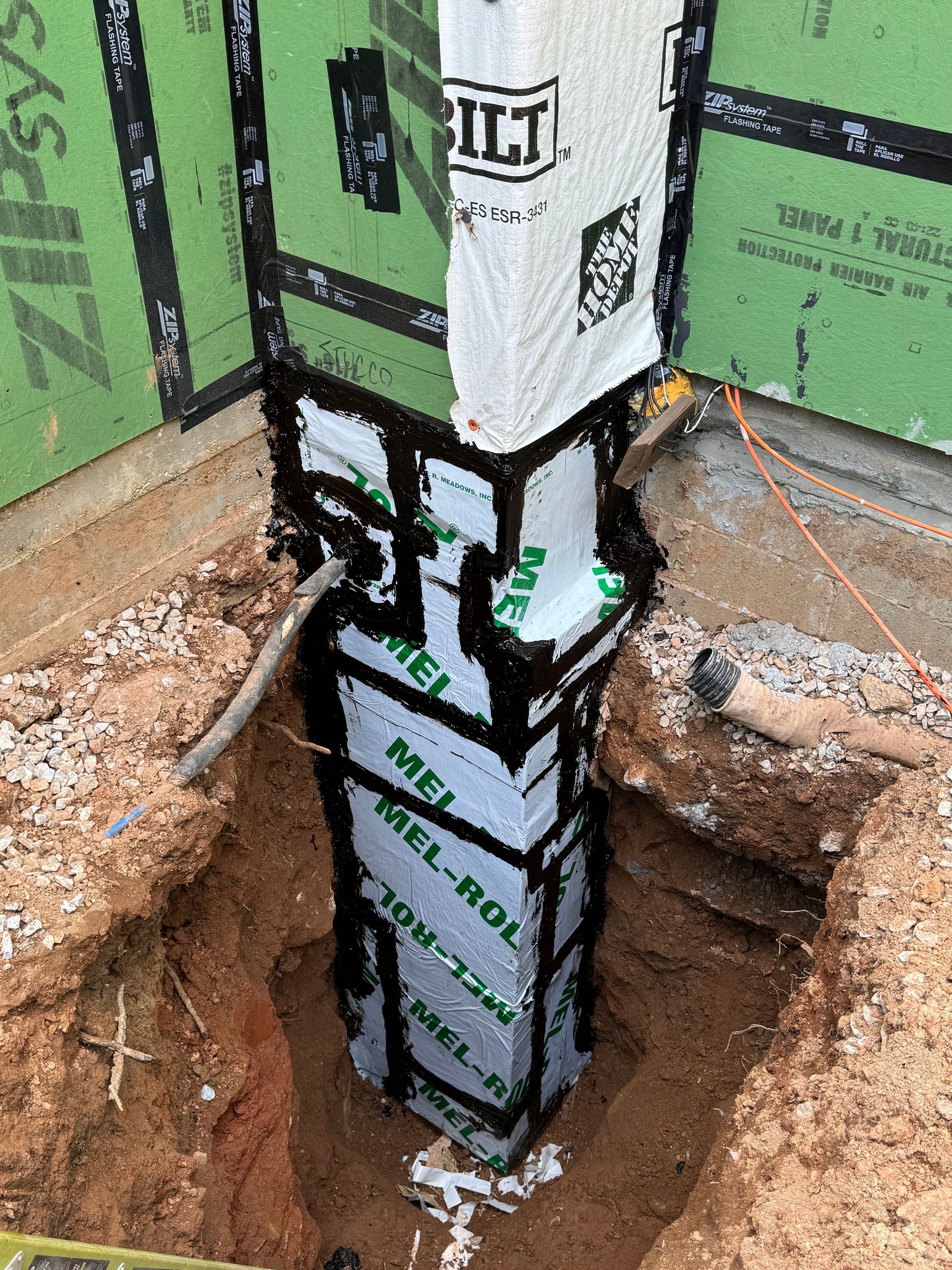 Foundation corner construction with black waterproofing membrane, insulation, and soil.